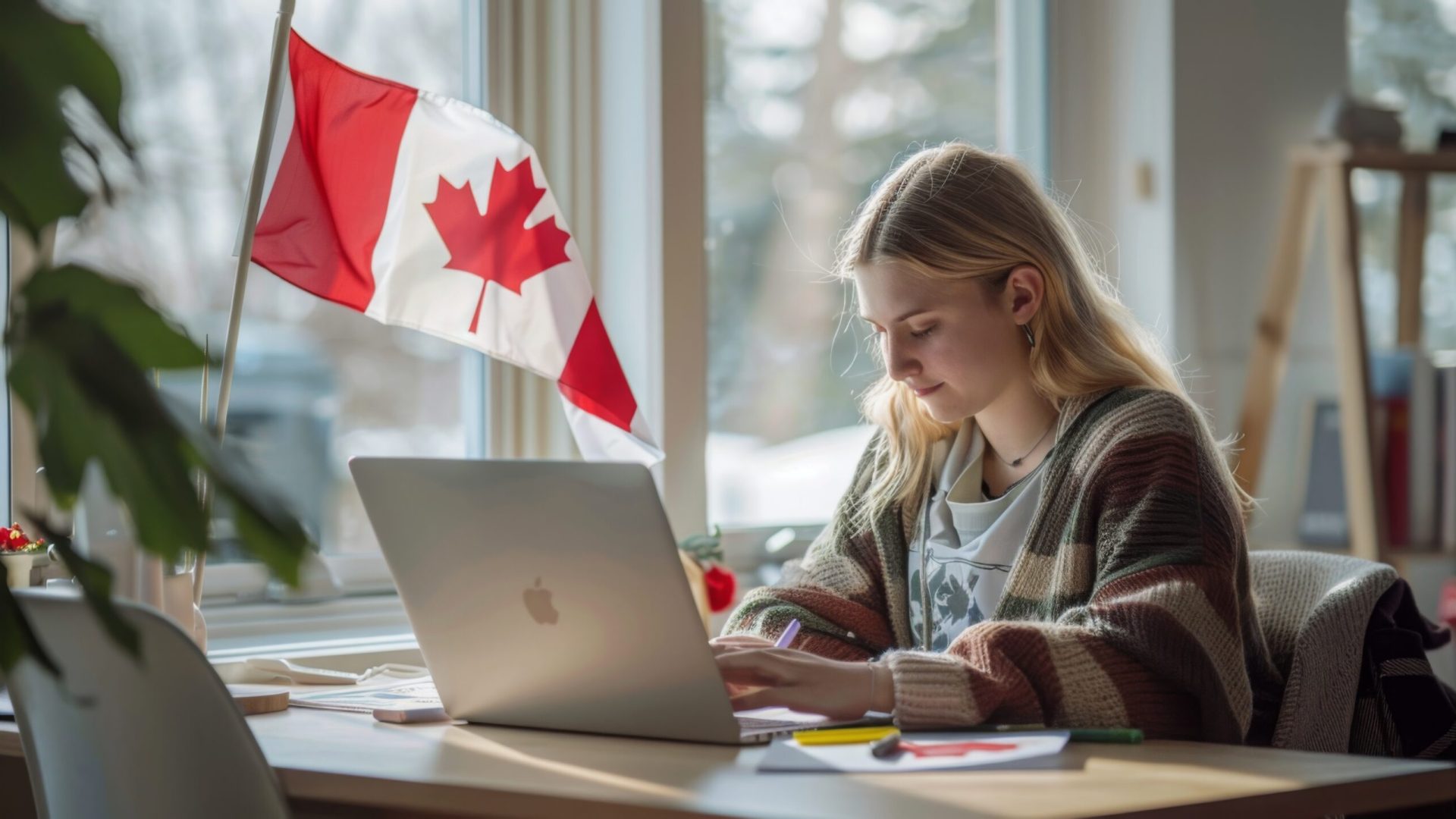 A student focuses on their laptop while seated at a desk decorated with a Canadian flag and stationery.