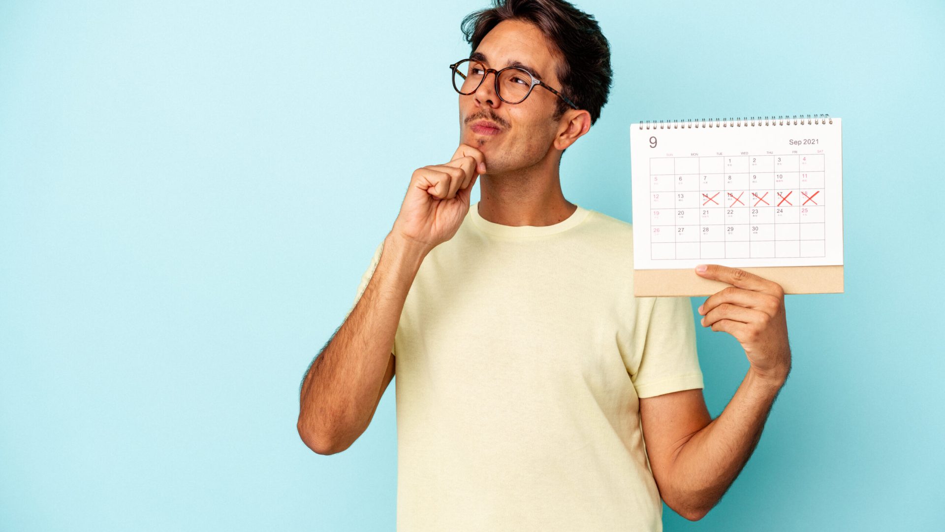 Young mixed race man holding calendar isolated on blue background looking sideways with doubtful and skeptical expression.