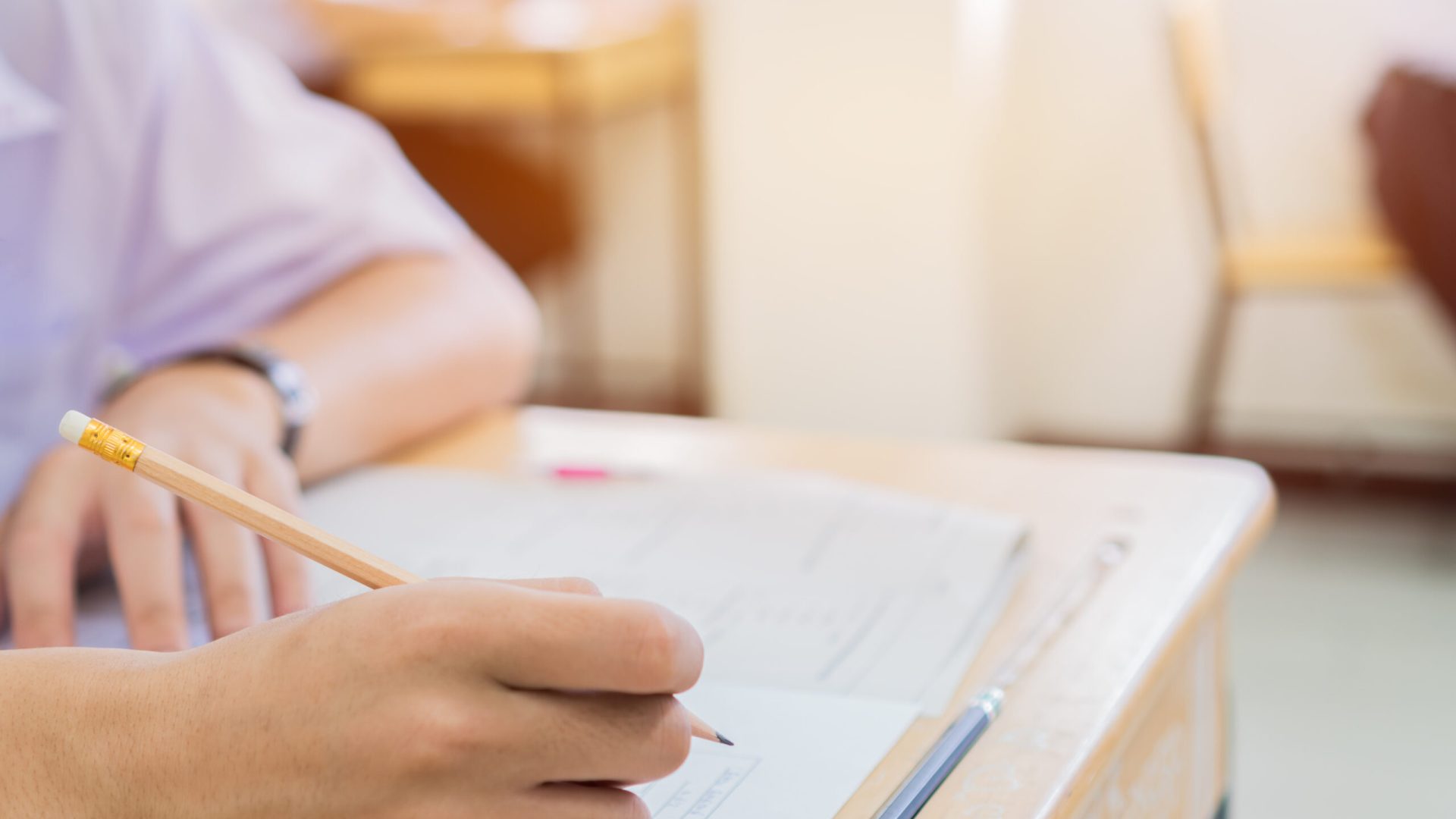 English exams test student in school, university students holding pencil for testing exam writing answer sheet or exercise for taking in assessment paper on table classroom. Education study Concept