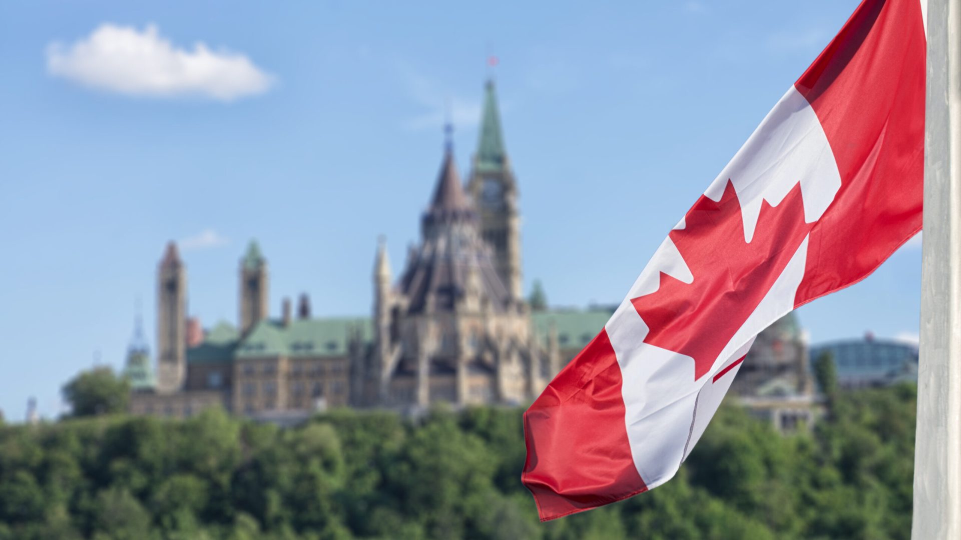 Canadian flag waving with Parliament Buildings hill and Library in the background