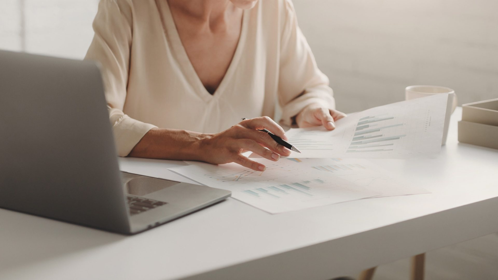 Close-up of a person reviewing documents and working on a laptop at a desk, indicating business or study