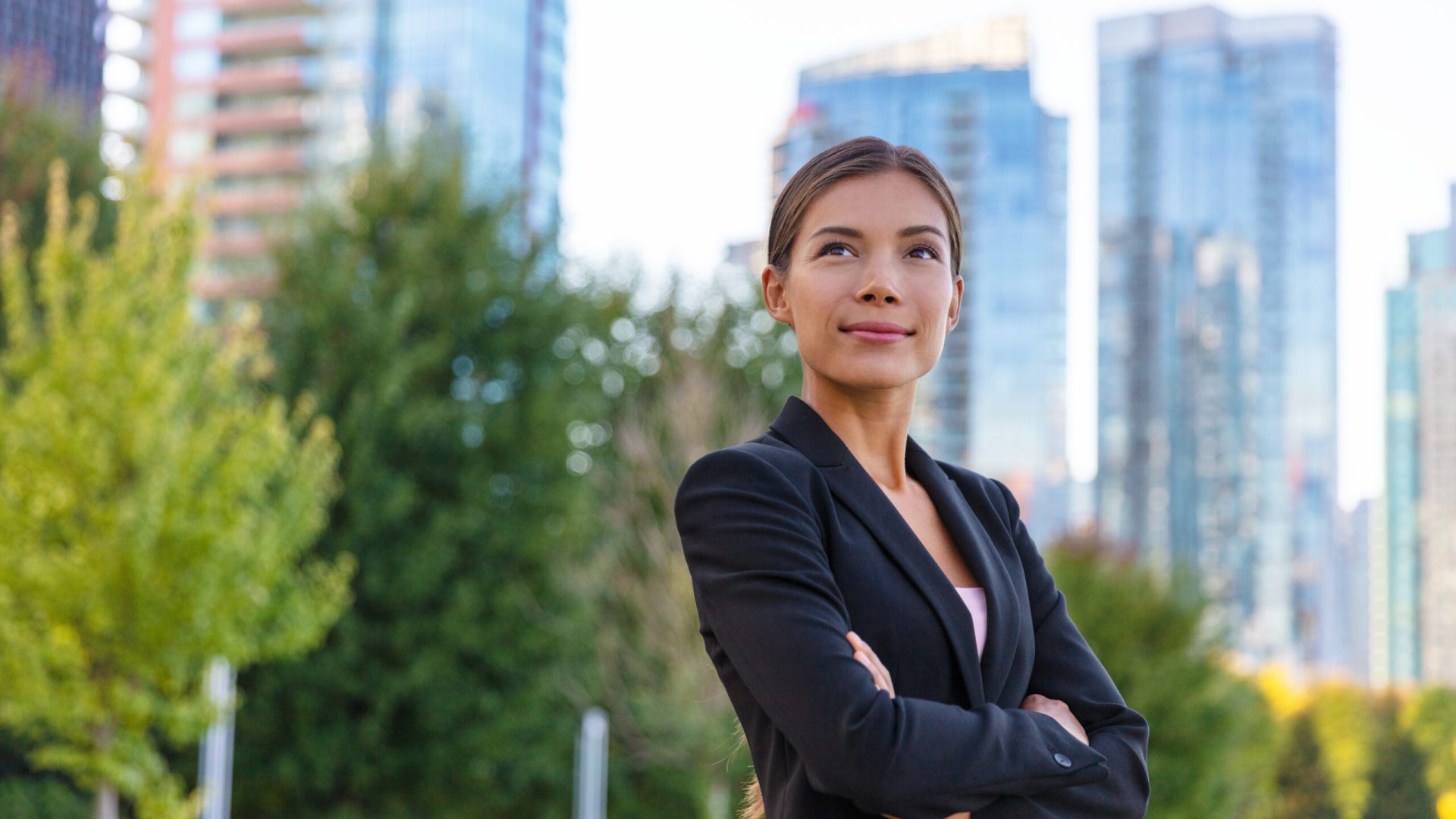 Asian businesswoman. Happy business woman portrait pensive looking up contemplative of her career. City job employment. Chinese professional in black suit confident with crossed arms.