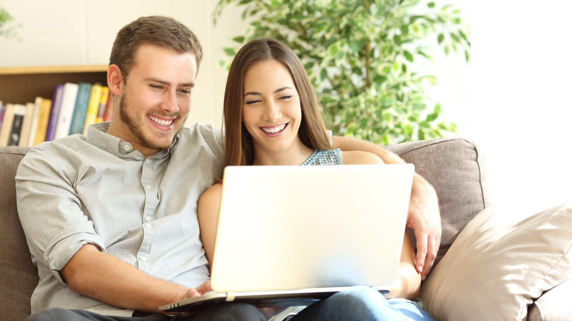 Happy couple using a laptop sitting on a couch in the living room at home
