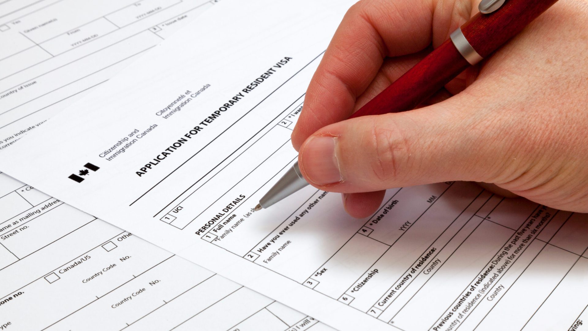 A man holding a ballpoint pen to fill a permanent residence visa application form to Canada.