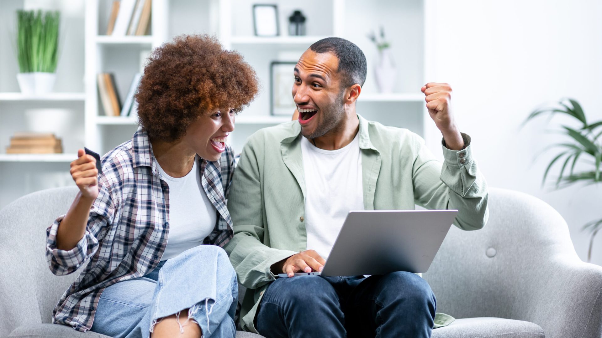 Joyful sincere laughing young african american family couple celebrating internet success, getting online lottery giveaway gambling auction win notification, feeling excited looking at laptop screen.