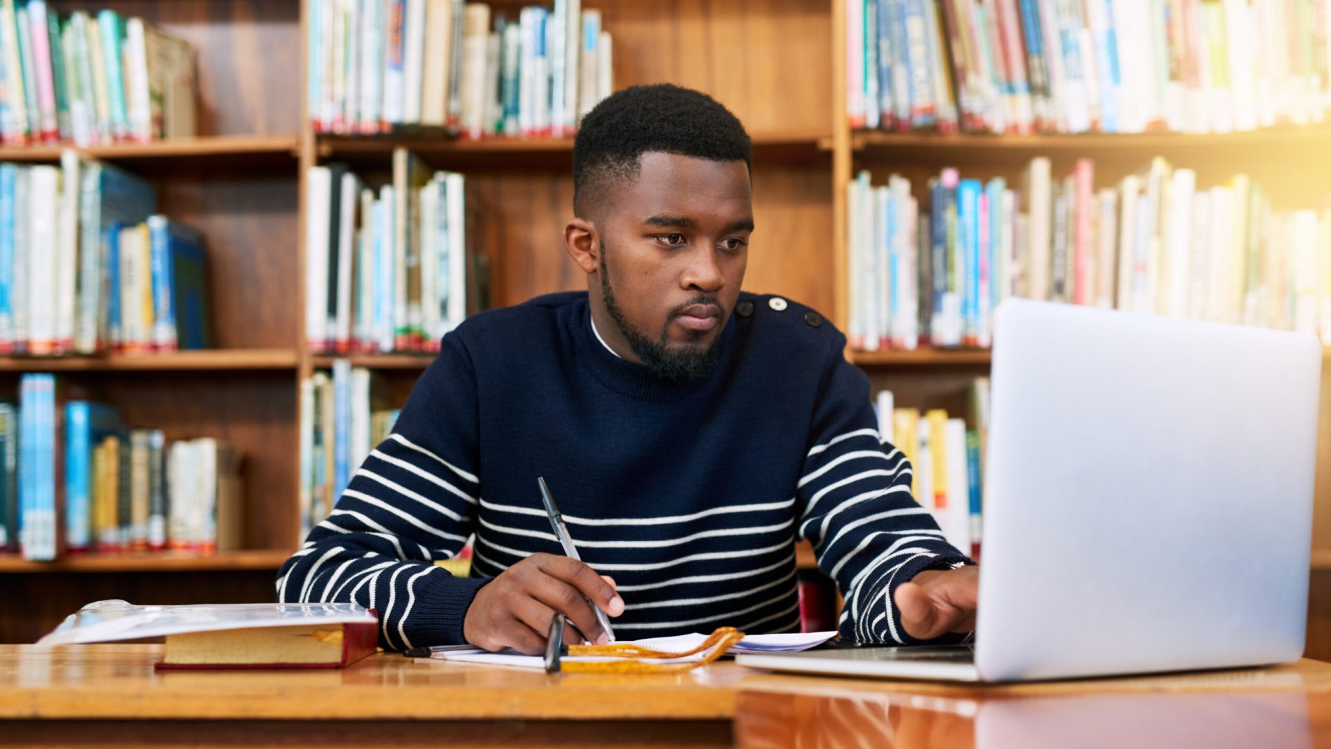 Laptop, library and university student with research, learning and planning for exam, report or focus on studying, goals and education. Black man, college and working on task, essay or scholarship.