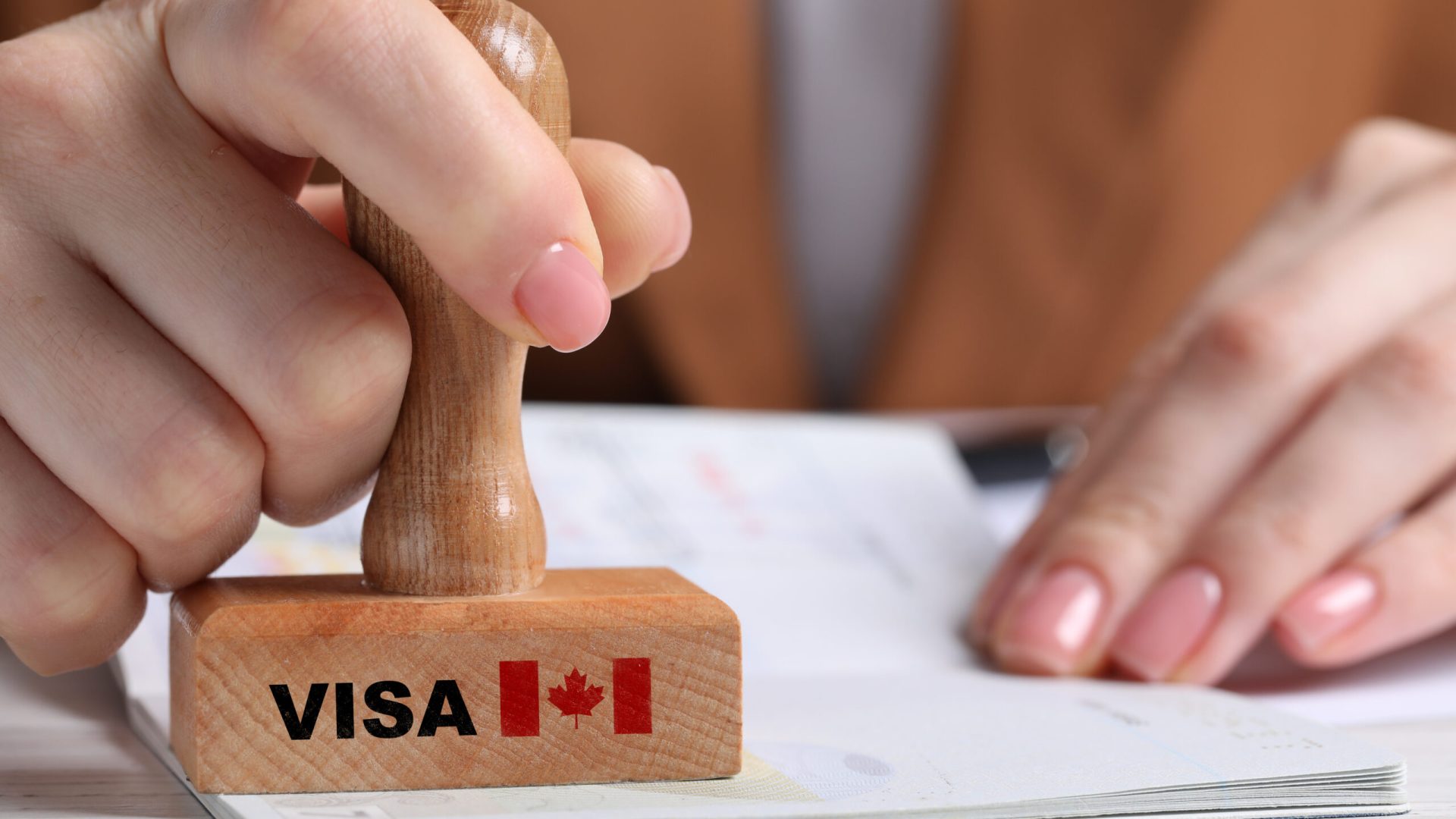 Woman stamping document at white wooden table, closeup. Visa for Canada