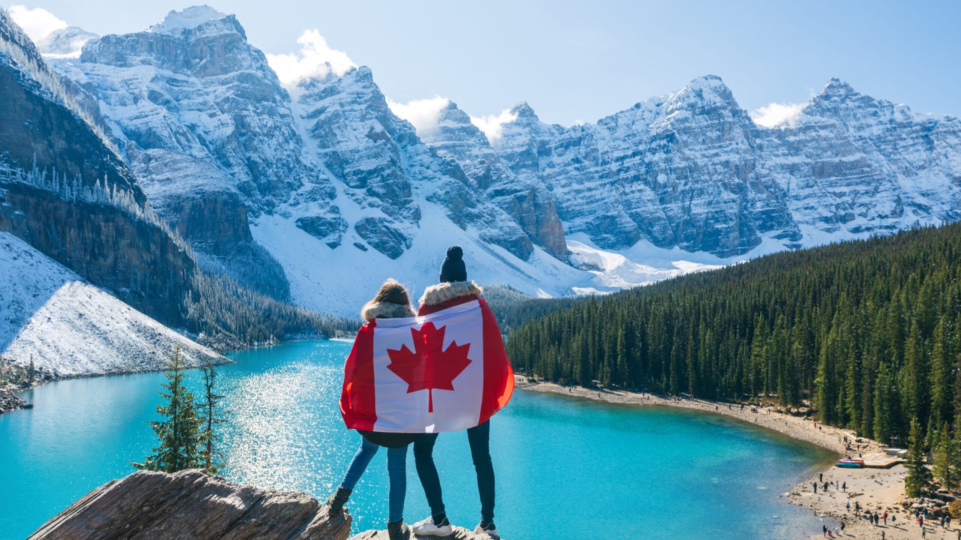Tourists draped in Canadian flag looking beautiful scenery of Moraine lake. Banff National Park. Canadian Rockies. Alberta, Canada.