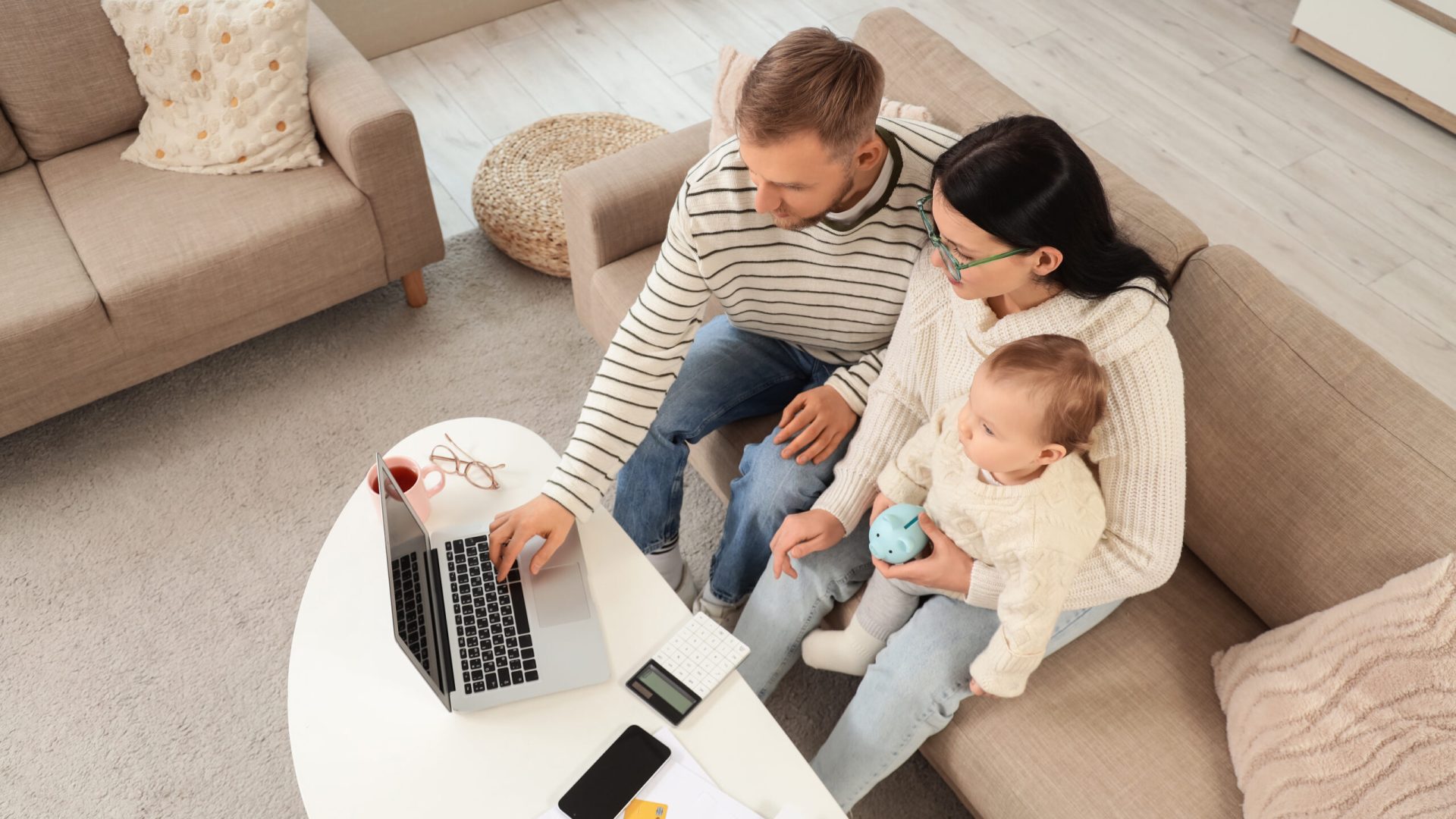 Young couple with their baby and laptop planning budget at home, top view